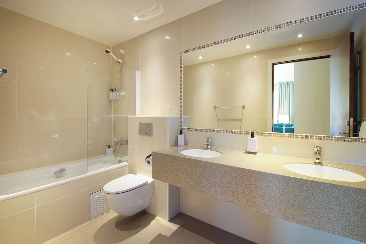 Een moderne badkamer met een bad, twee wastafels en een grote spiegel.