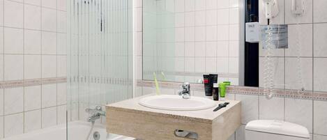 Un baño moderno con ducha envuelta en vidrio, lavamanos con artículos de aseo y un inodoro.