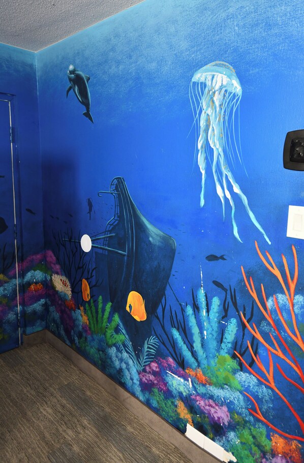 A mural of an underwater scene with a dolphin, jellyfish, and coral on a wall.