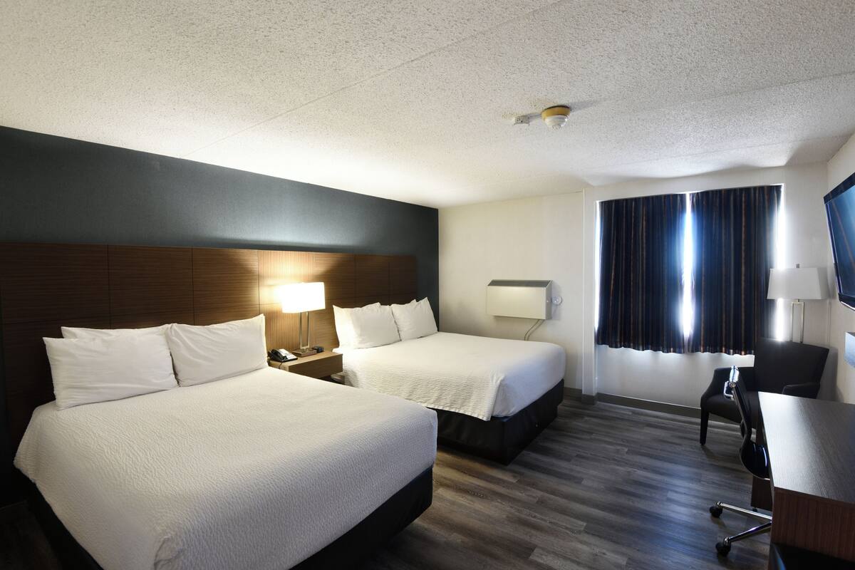 A hotel room with two beds, a desk, a chair, a TV, and a window with curtains.