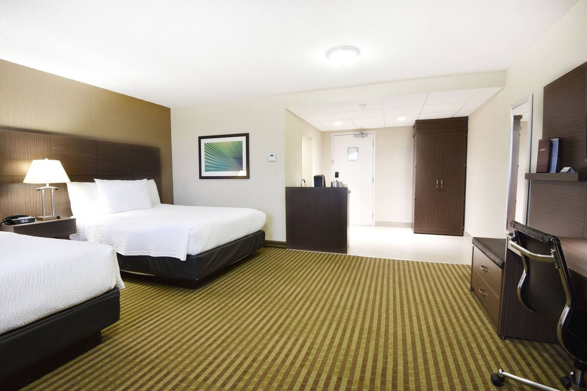 A hotel room with two beds, a desk, a dresser, and a mirror.