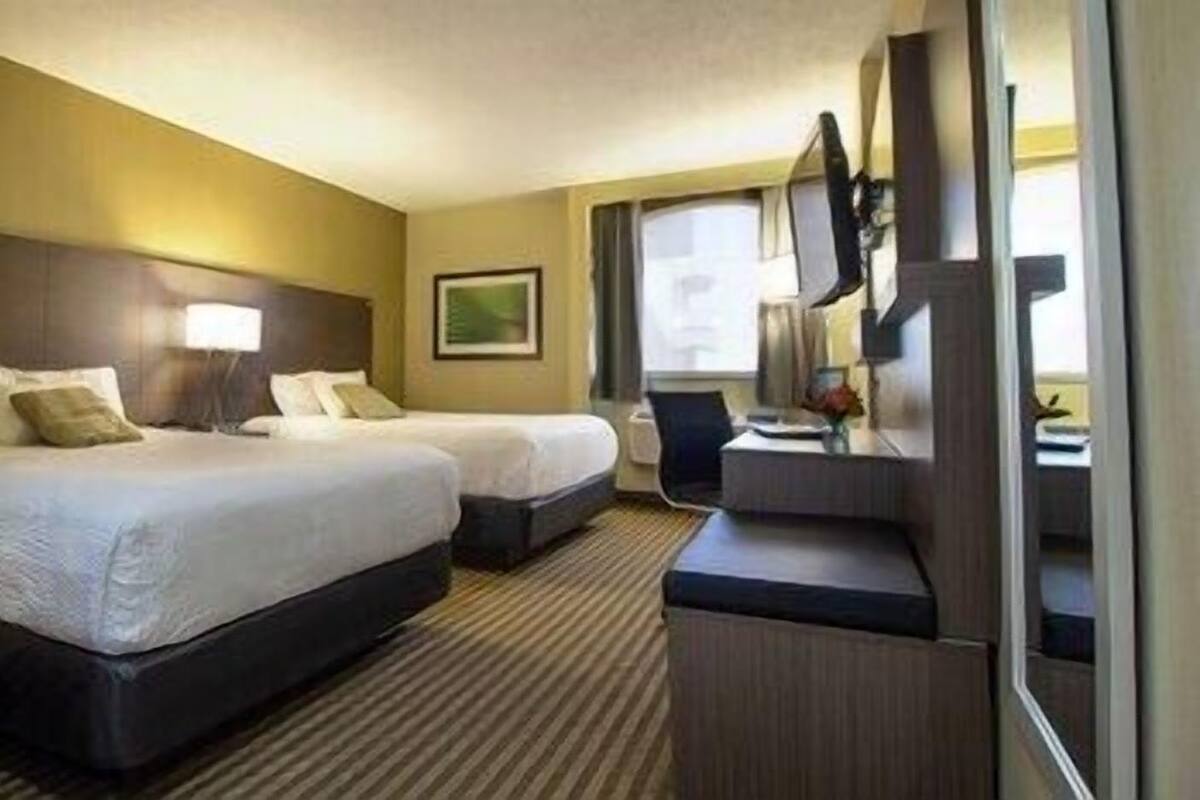 A hotel room with two beds, a desk, a chair, a lamp, a painting, and a window.