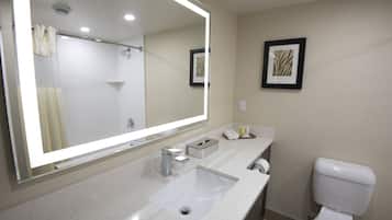 A modern bathroom with a large mirror, a sink, a toilet, and framed artwork on the wall.