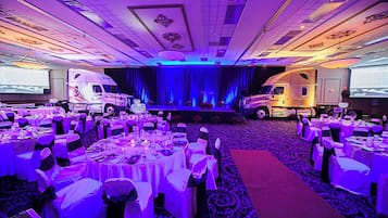 A banquet hall with round tables, chairs, and a stage.