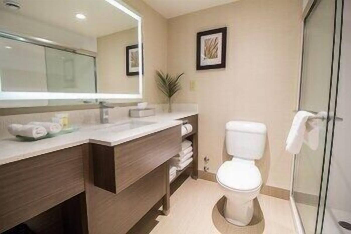 A modern bathroom with a large mirror, a toilet, a shower area, and a vanity with towels.
