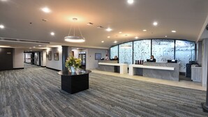 A modern hotel lobby with a reception desk, a large vase with flowers, and a patterned wall. - Victoria Inn Hotel and Convention Centre Winnipeg (Winnipeg)