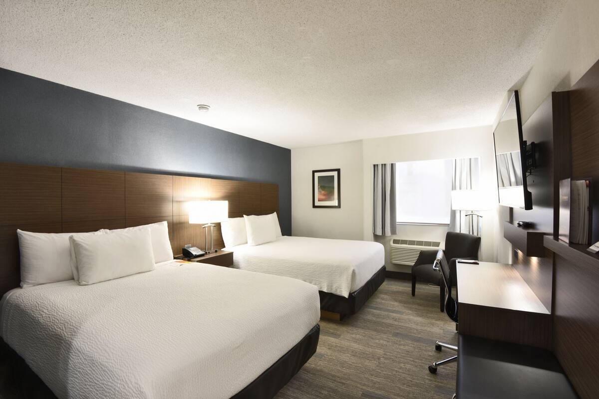 A hotel room with two beds, a desk, a chair, a lamp, and a picture on the wall.