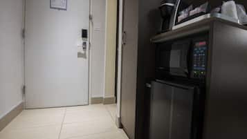A hotel room with a microwave, refrigerator, and a door with a light switch.