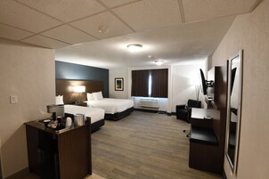 Una habitación de hotel con cama, escritorio, silla, televisor y ventana con cortinas.