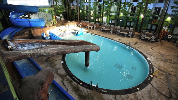 An indoor pool with a slide, seating area, and a mural of trees. - Victoria Inn Hotel and Convention Centre Winnipeg (Winnipeg)
