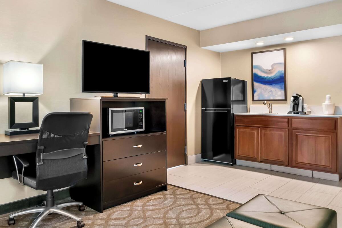 Hotelkamer met een bureau, bureaustoel, flatscreen televisie, magnetron, koelkast en houten kasten.
