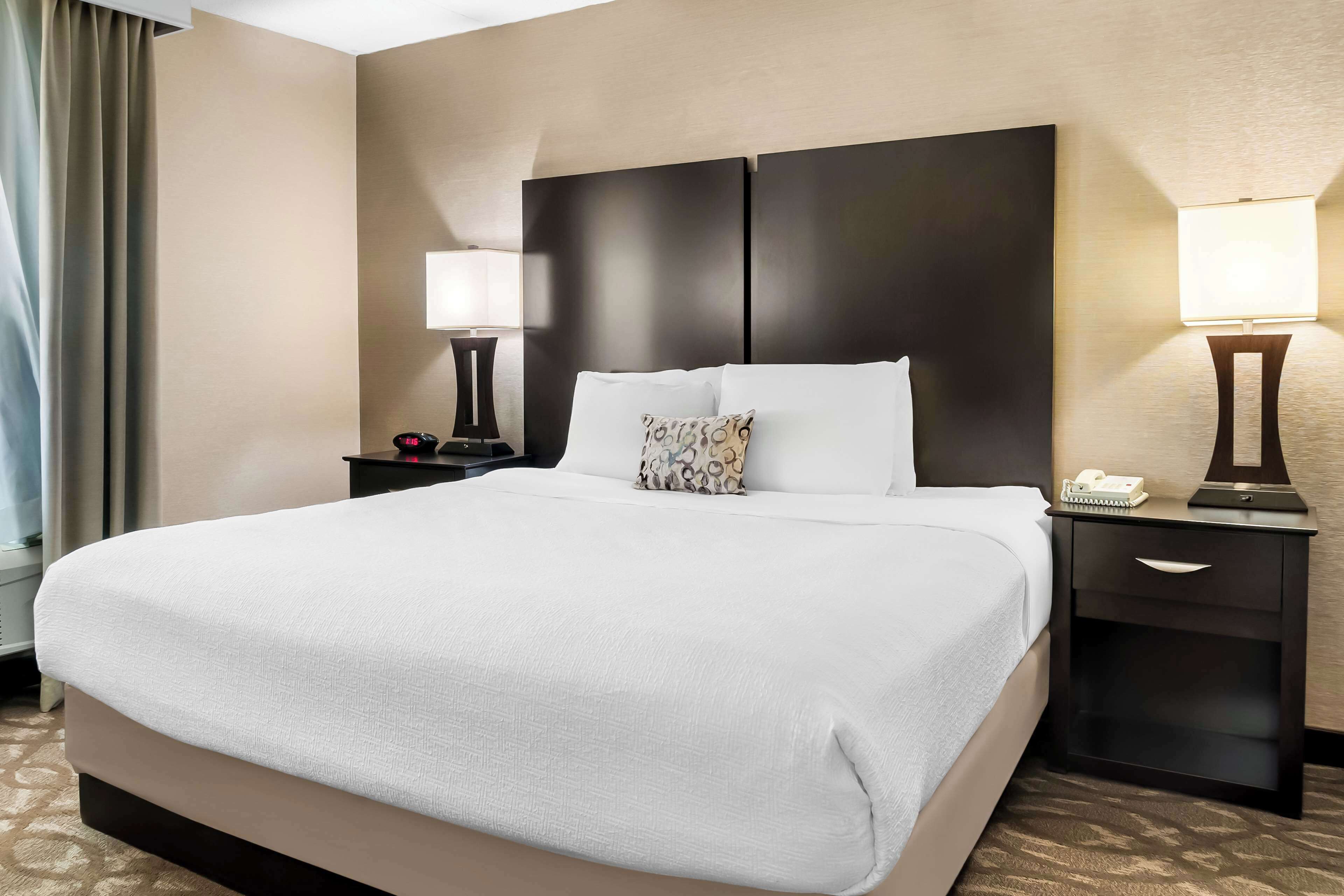 Habitación de hotel con una cama grande, dos mesitas de noche con lámparas, cabecera y alfombra estampada.
