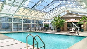 Une piscine intérieure dotée d’un toit en verre transparent, de chaises longues et de parasols.