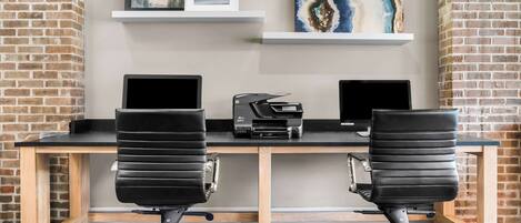 A modern office desk with two black office chairs, two laptops, and a printer.