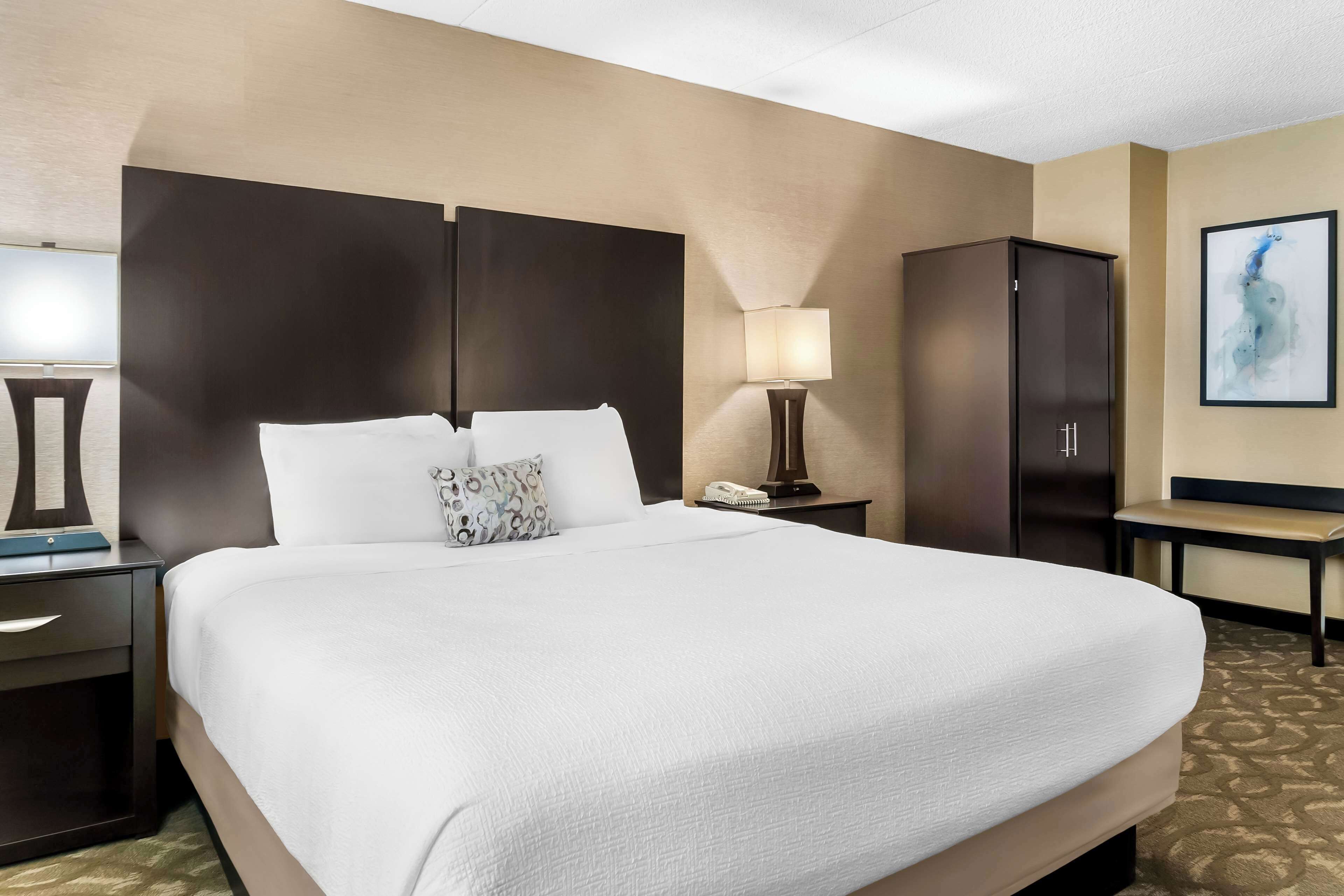 A hotel room with a large bed, a nightstand with a lamp, a wardrobe, and a framed picture on the wall.