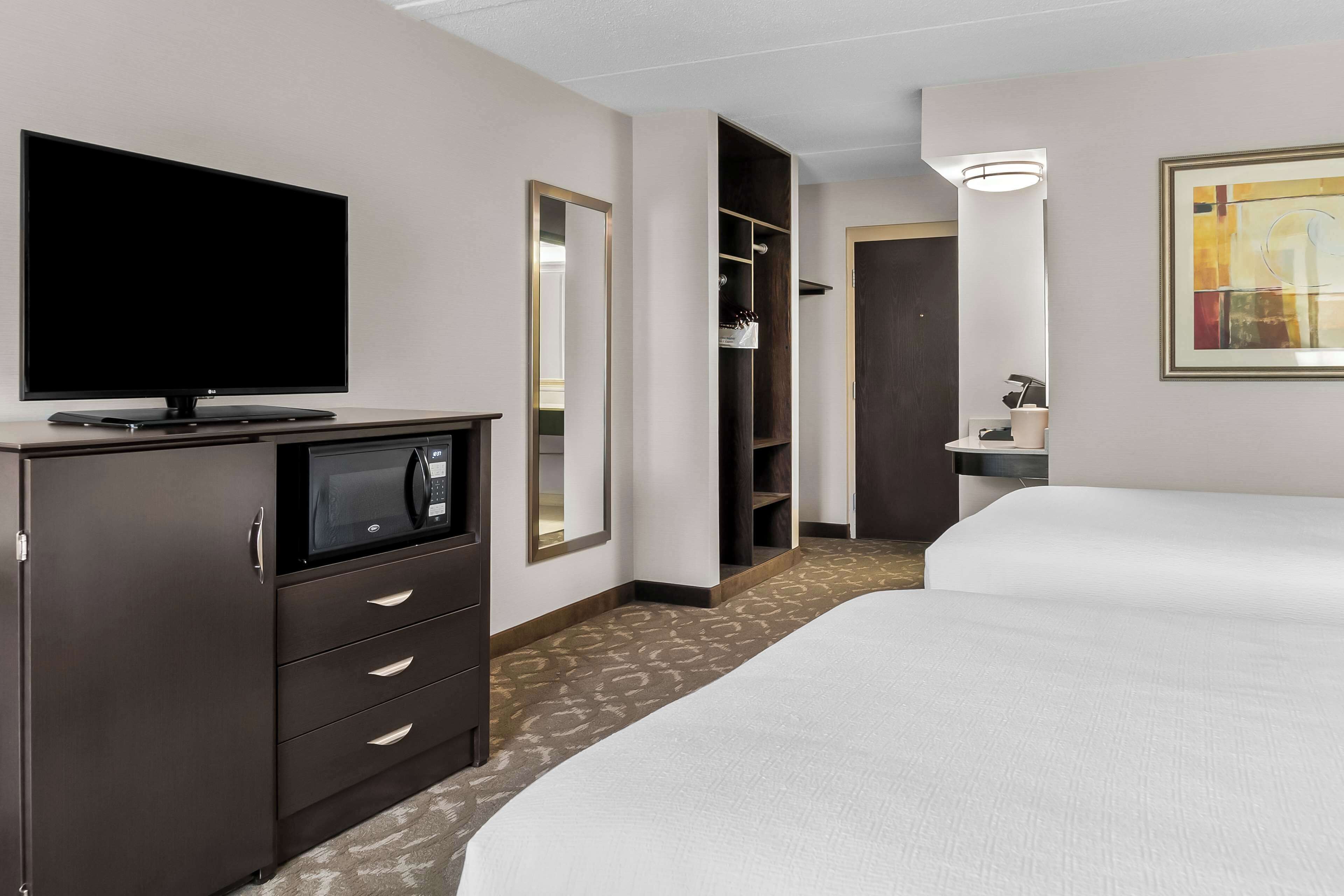 Une chambre d’hôtel équipée d’une télévision à écran plat, d’un four à micro-ondes, d’une armoire, d’un placard, d’une table de chevet et d’un lit.