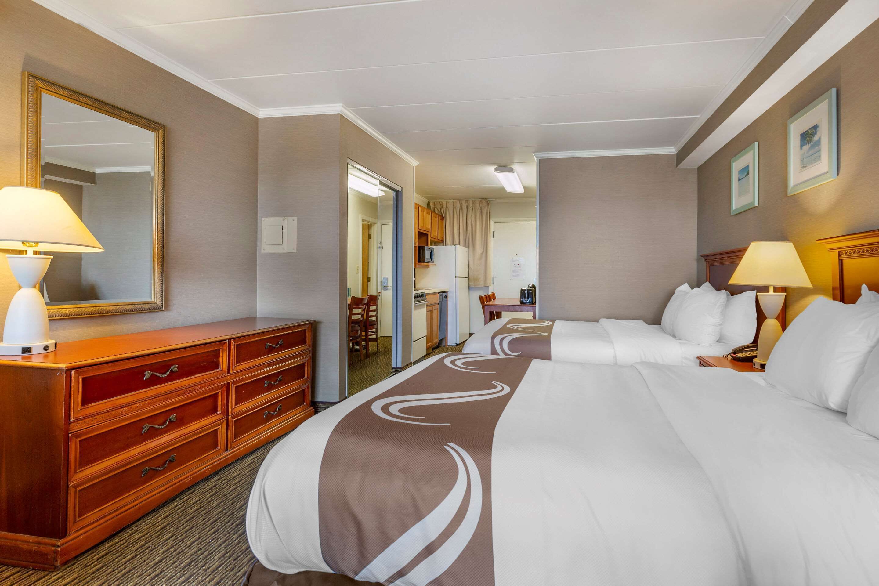 A hotel room with a large bed, a wooden dresser, a mirror, and a desk with a lamp.