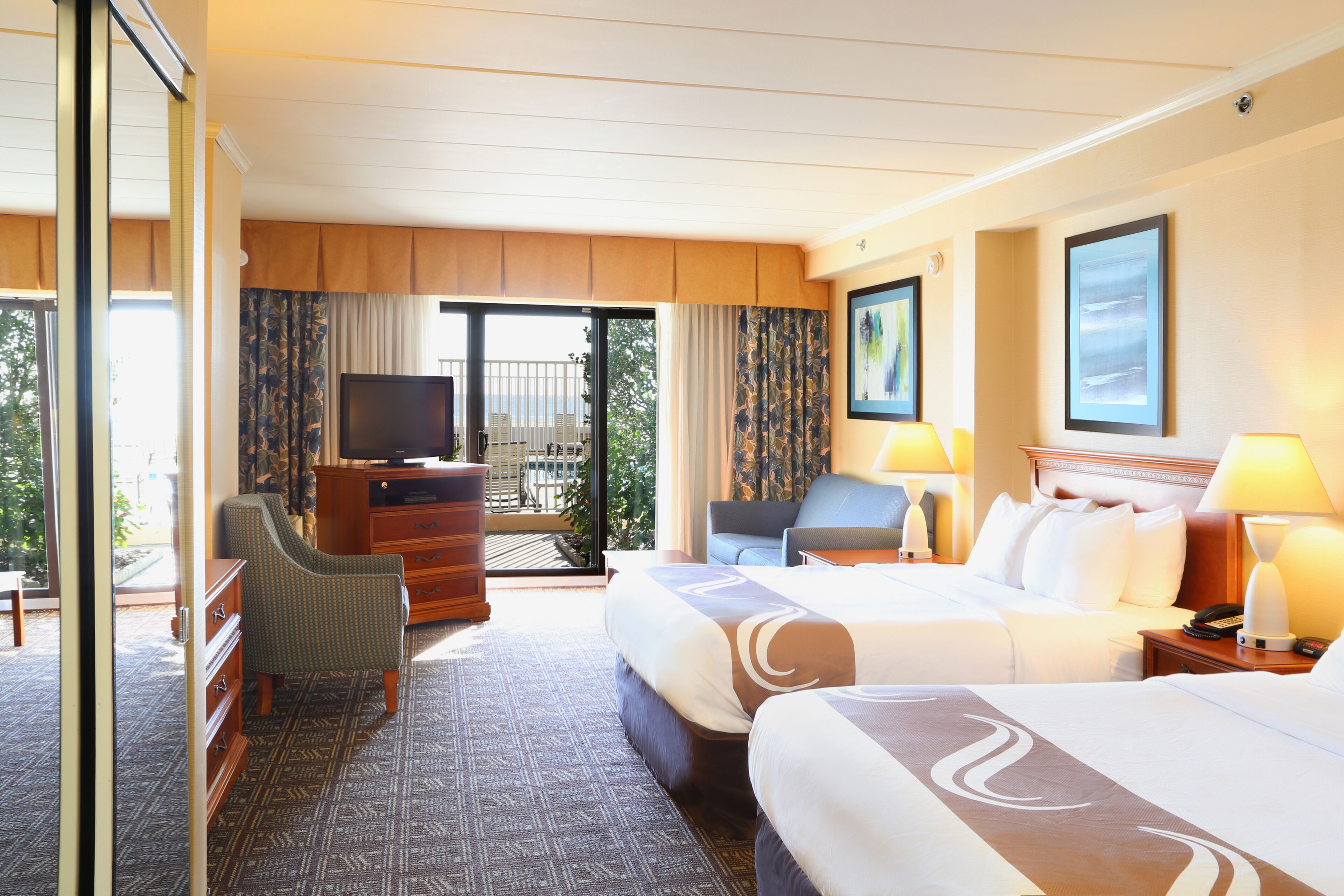 A hotel room with two beds, a TV, a desk, and a balcony with a view.