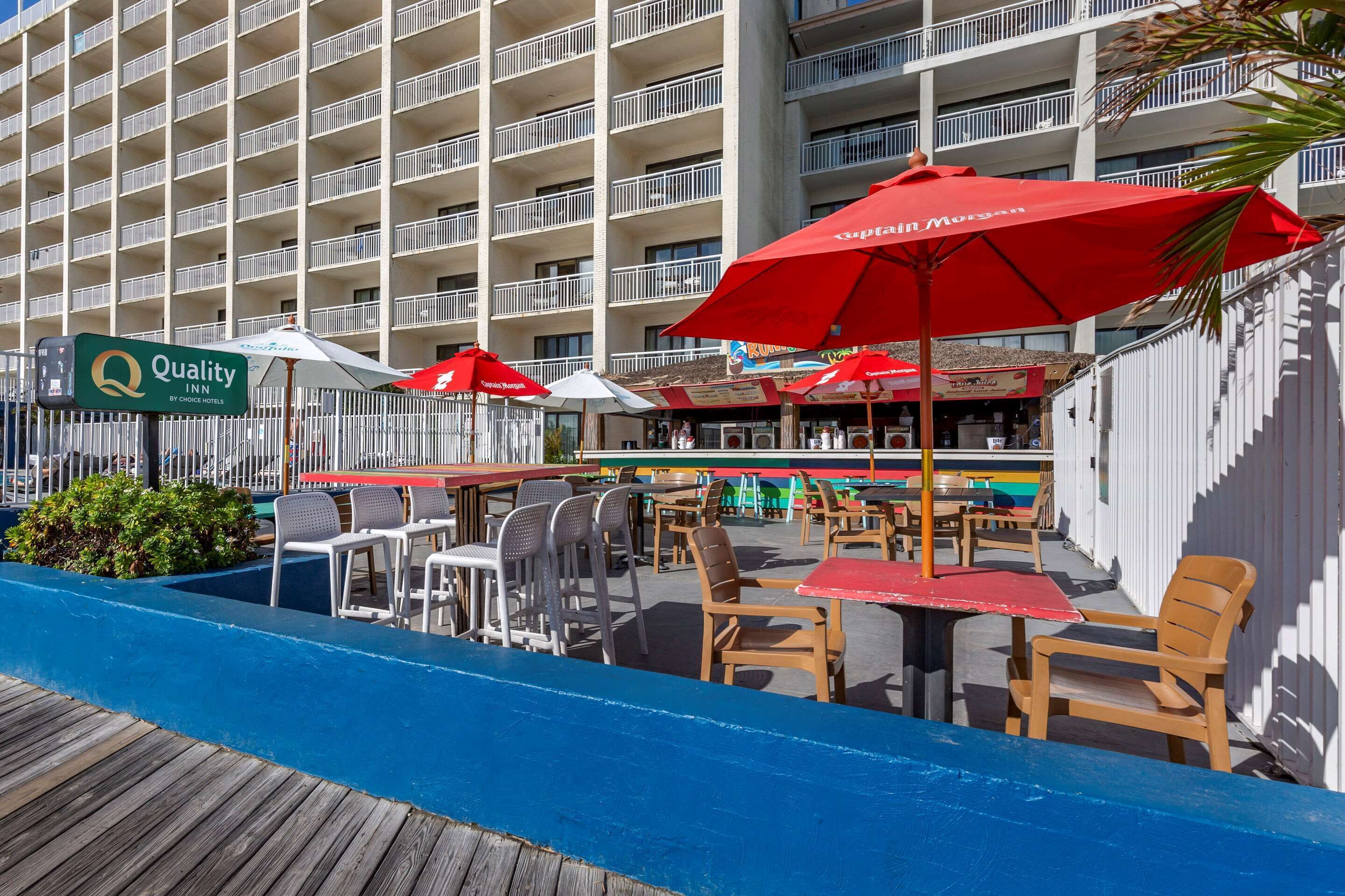 Un patio de hotel con mobiliario exterior, sombrillas rojas y un letrero de Quality Inn by Choice Hotels.