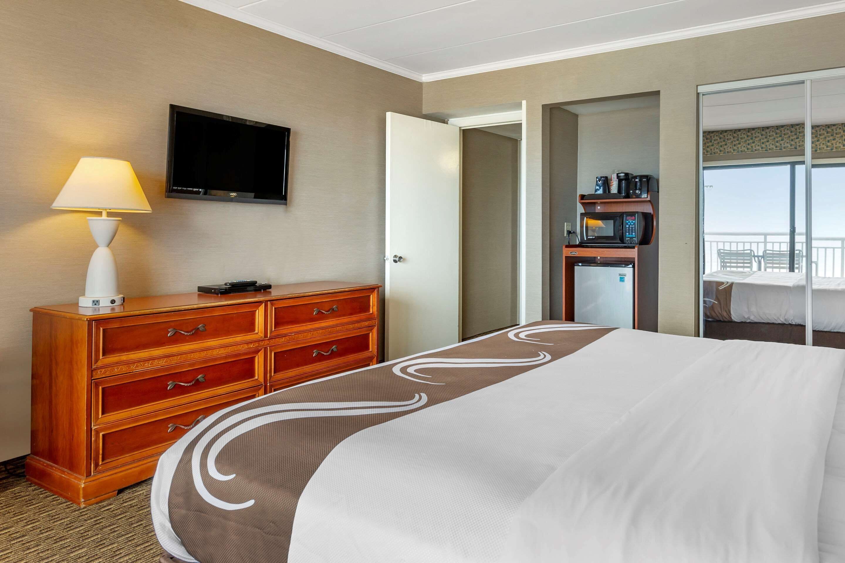 A hotel room with a bed, a TV mounted on the wall, a wooden dresser, a coffee maker, and a balcony with a view.