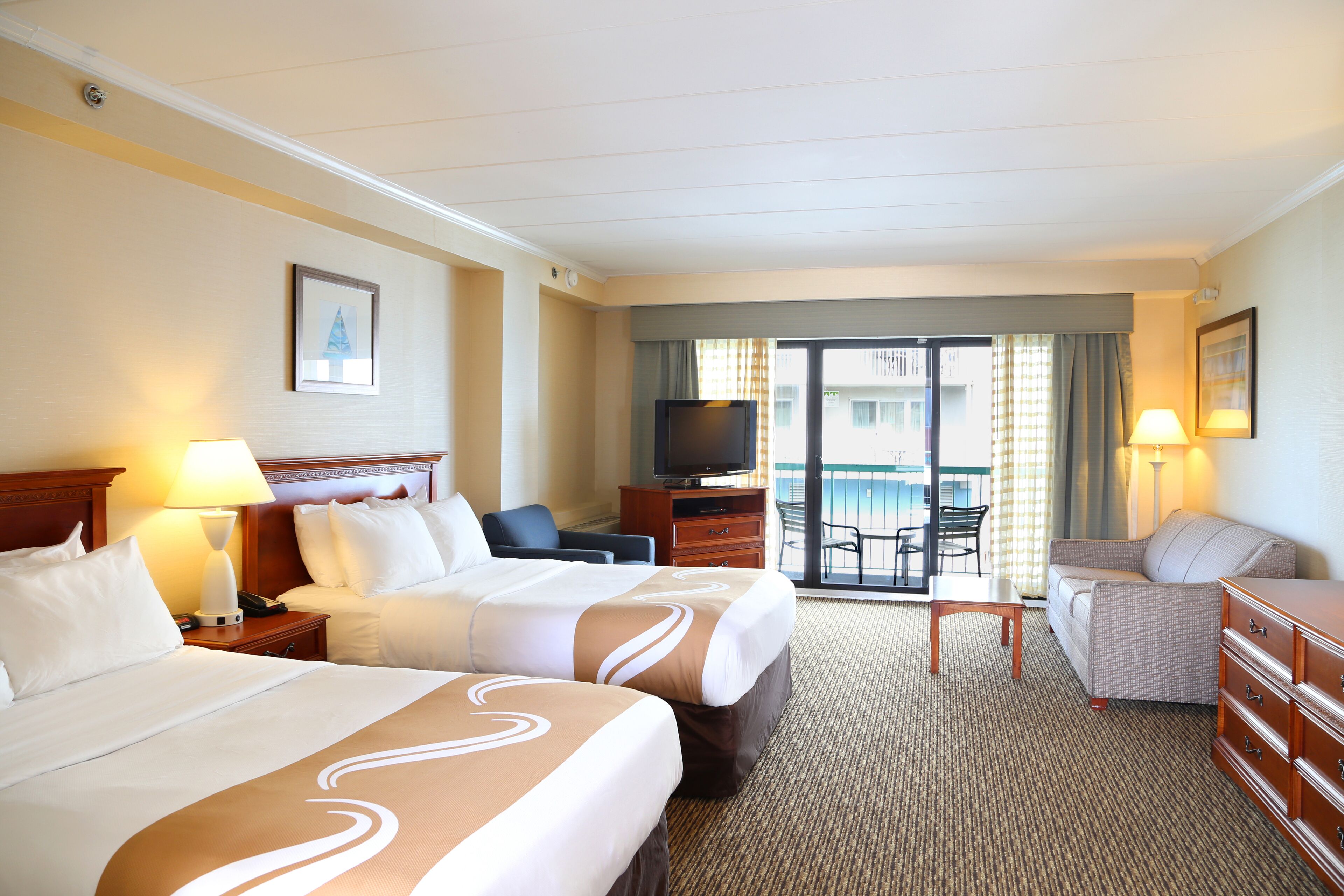 A hotel room with two beds, a television, a desk, and a view of the outside.