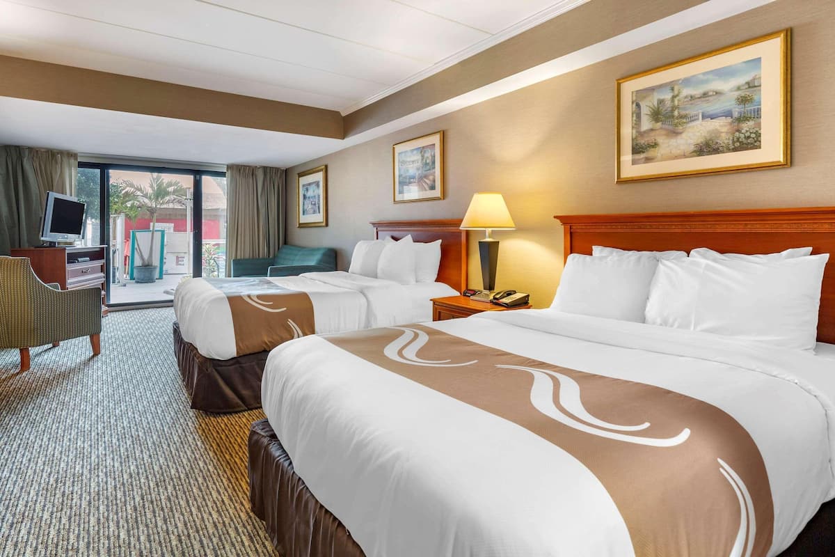 Une chambre d’hôtel avec deux lits, un bureau avec un ordinateur, une chaise, une lampe et un tableau au mur.