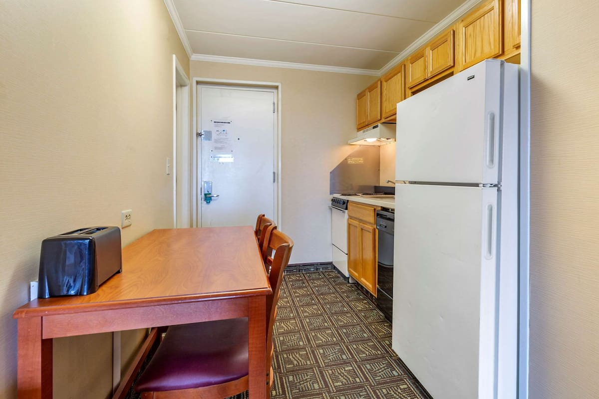 Une cuisine de taille réduite avec une table en bois, des chaises, un réfrigérateur blanc et des placards en bois.