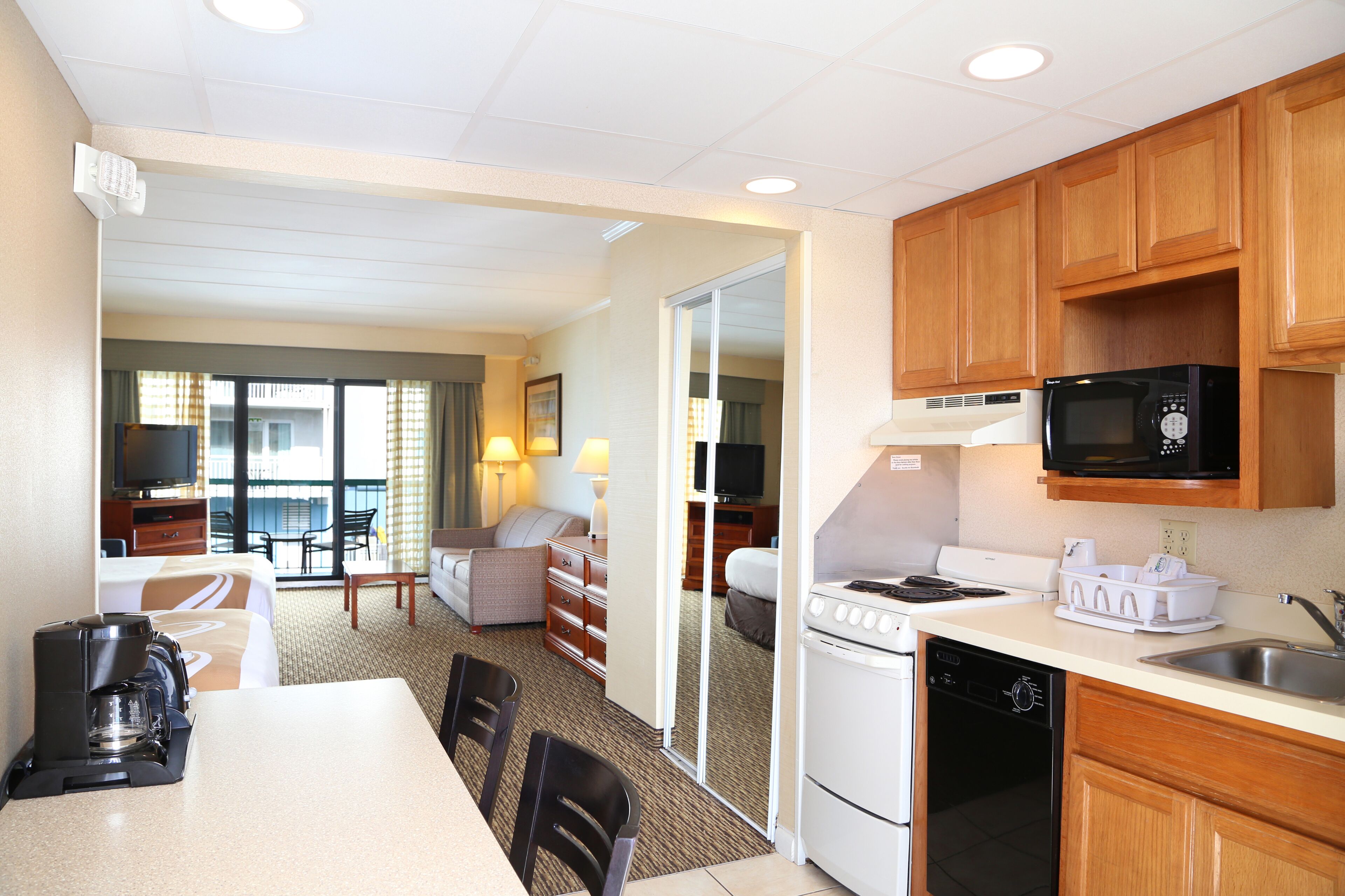 A hotel room with a kitchenette, a dining area, a sofa, and a television.