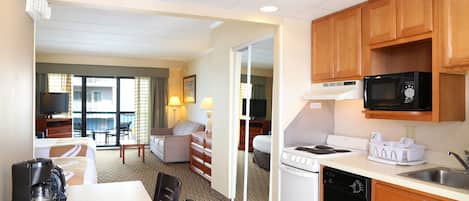 A hotel room with a kitchenette, a dining area, a sofa, and a television.