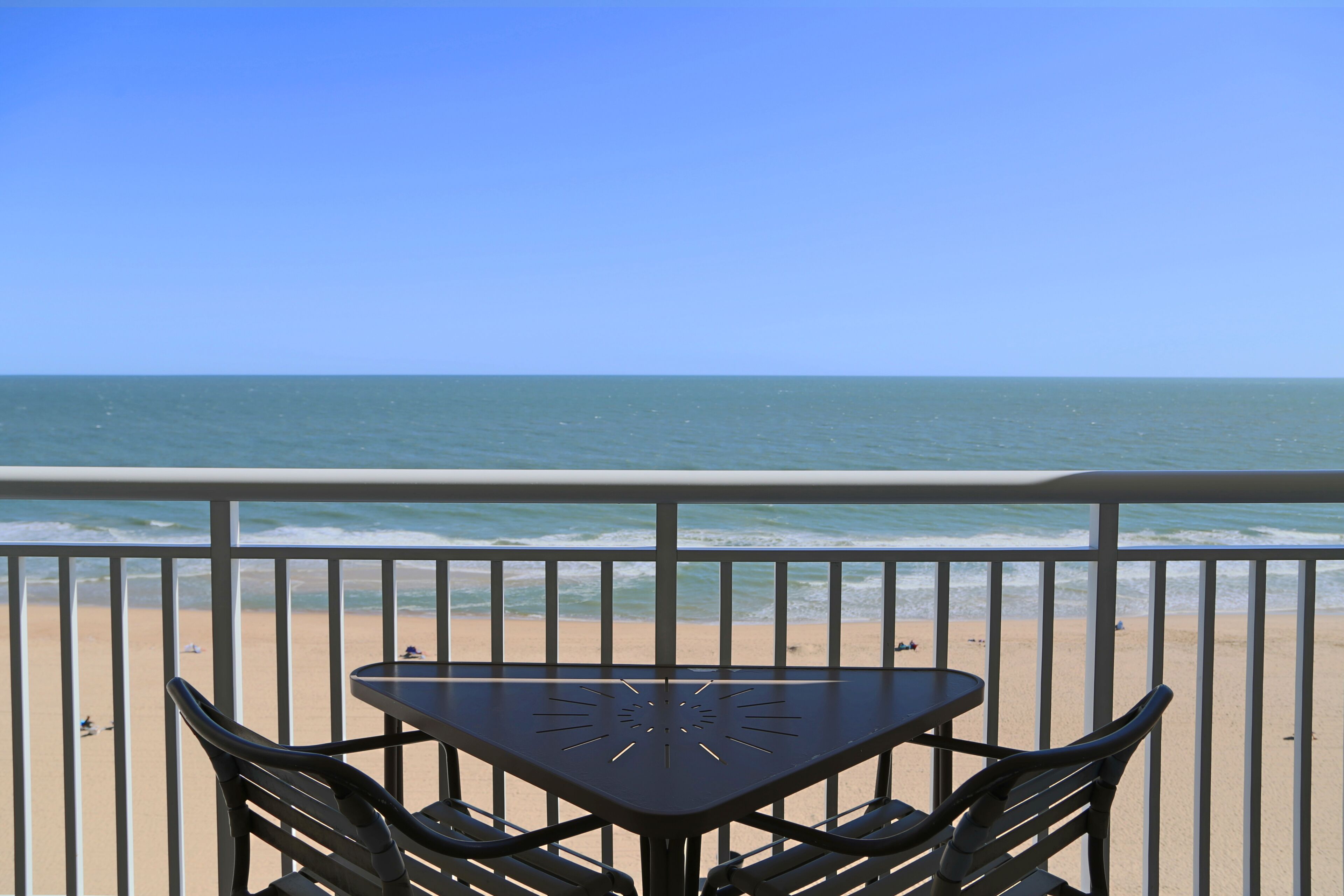 Ein Tisch und Stühle auf einem Balkon mit Blick auf einen Strand und Wellen.