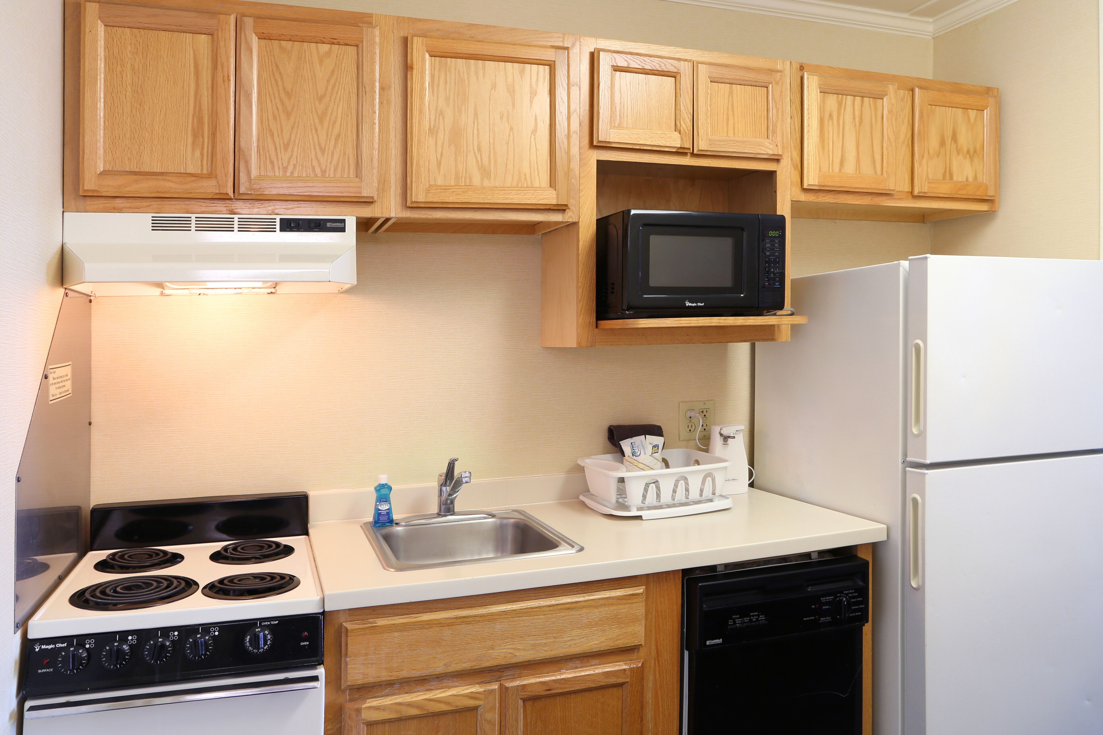 A kitchen with wooden cabinets, a microwave, a stove, a sink, and a dishwasher.