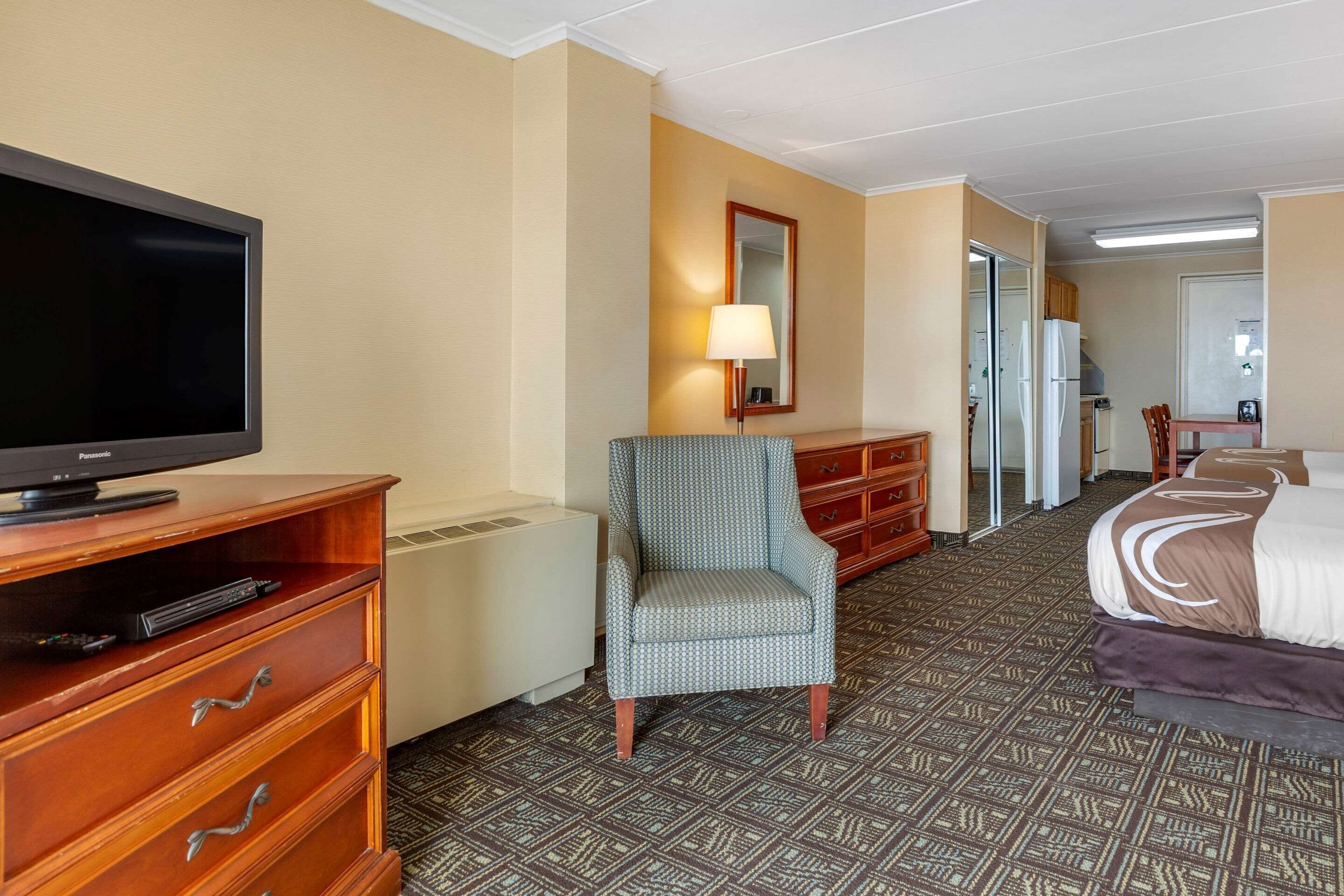 Una habitación de hotel con televisión, una silla, una cama, un aparador y un espejo.