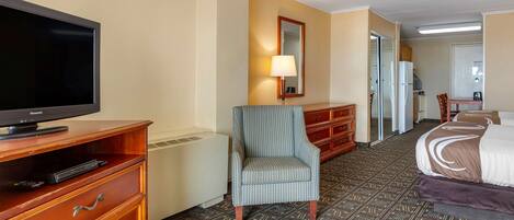 Una habitación de hotel con televisión, una silla, una cama, un aparador y un espejo.