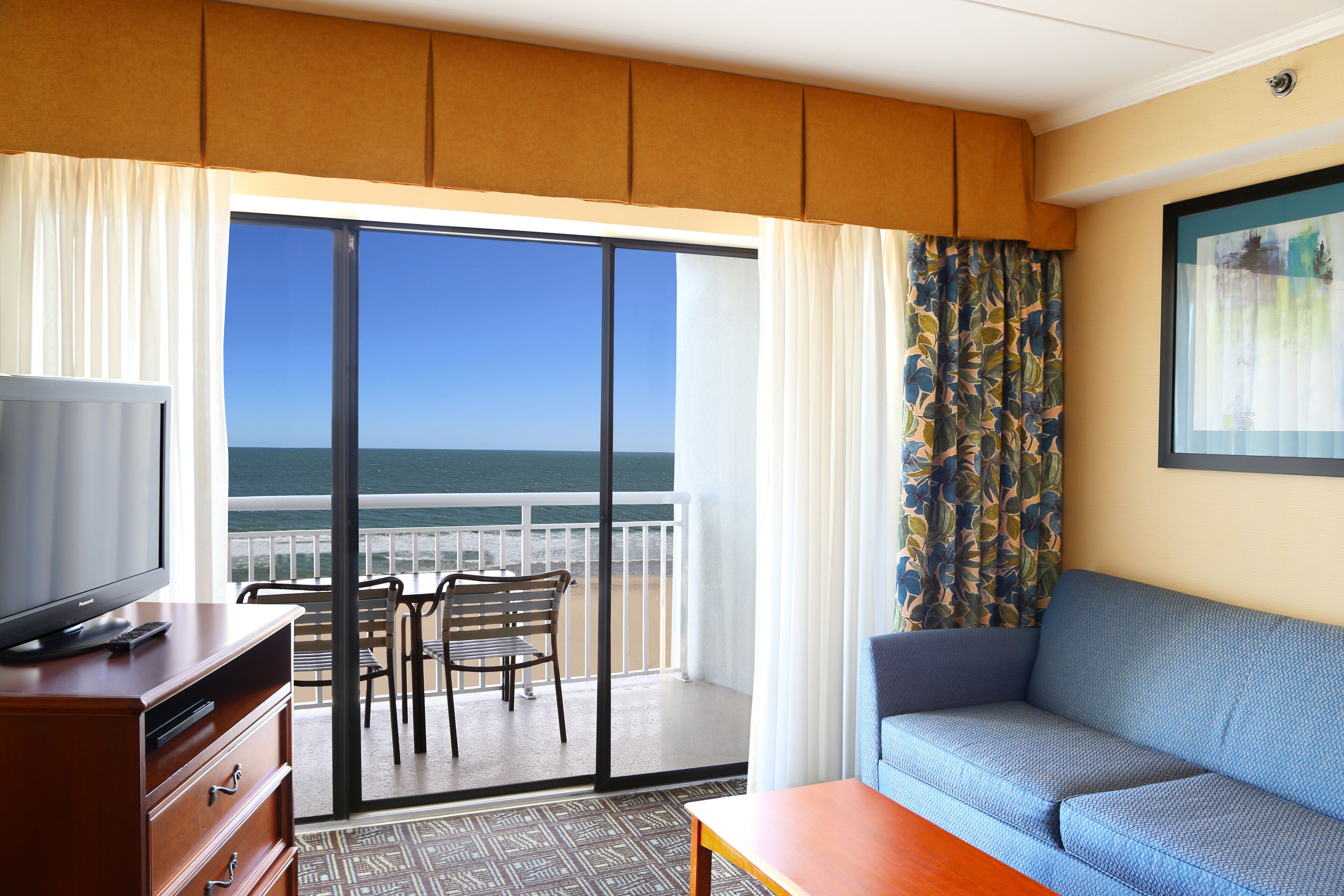 Habitación de hotel con balcón, sofá, televisión y zona de comedor.