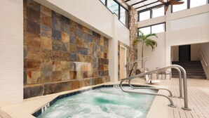A hot tub with a stone wall backdrop, indoor stairs, and a palm tree. - Quality Inn Boardwalk (Ocean City)