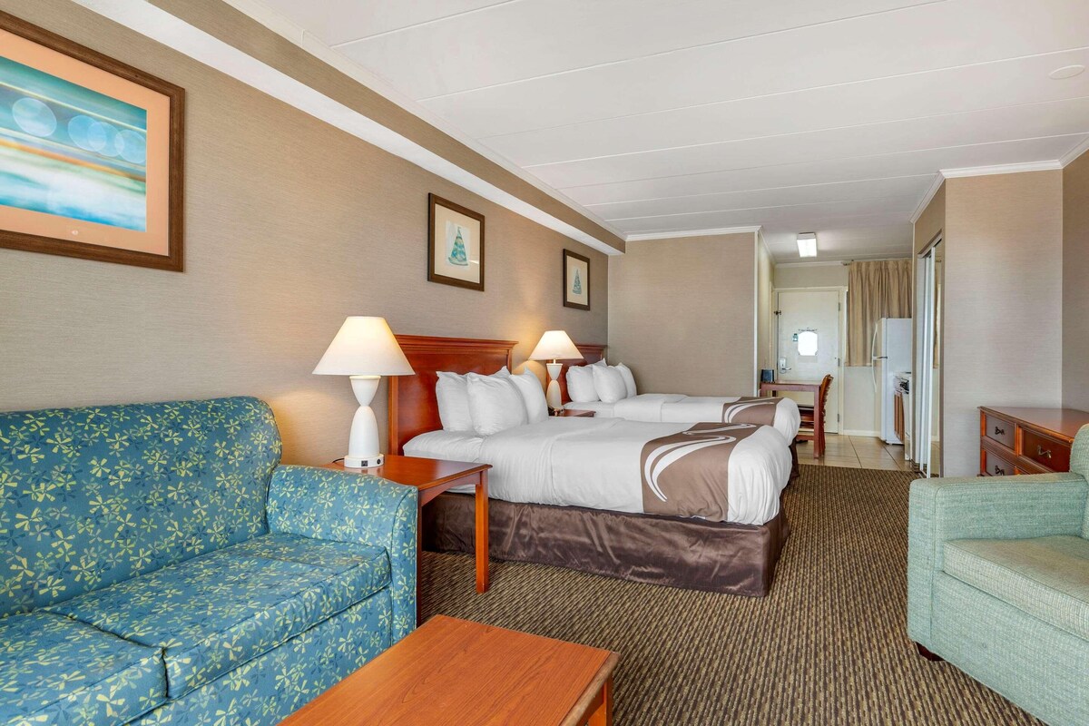 A hotel room with a sofa, two beds, a desk, and a chair.