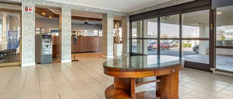 A lobby with a round wooden table, an ATM, and a glass door leading outside.