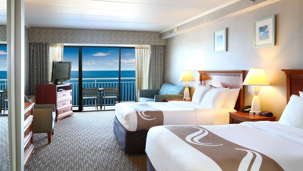A hotel room with two beds, a desk, a chair, a TV, and a view of the ocean. - Quality Inn Boardwalk (Ocean City)