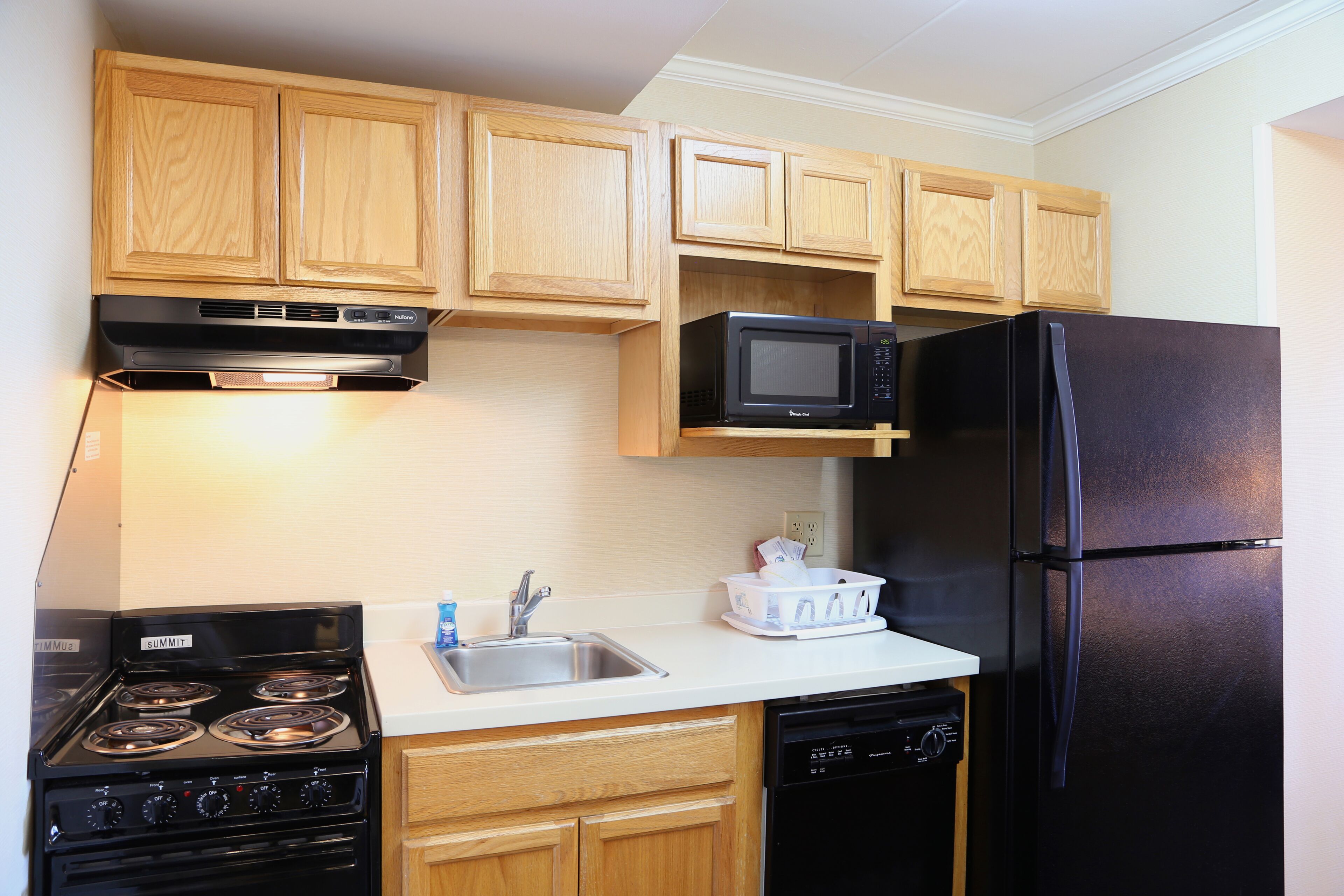 Une cuisine avec des meubles de rangement en bois, une cuisinière noire, un four à micro-ondes, un réfrigérateur et un lave-vaisselle.