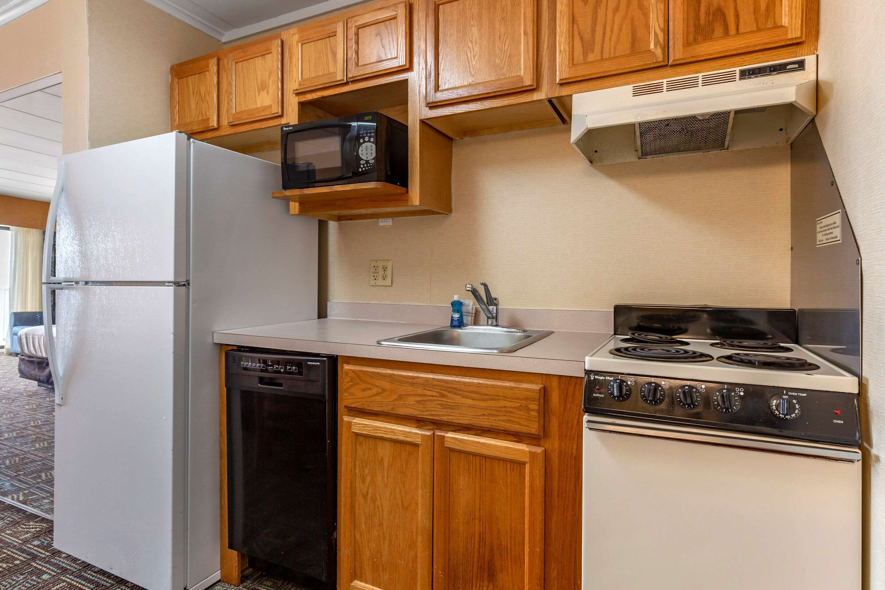 A compact kitchen with wooden cabinets, a white refrigerator, a dishwasher, a microwave, and a stove.