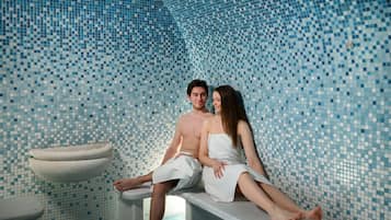 A couple sitting on a bench in a room with mosaic tile walls and a sink.