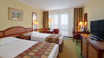 A hotel room with two beds, a desk with a TV, a chair, a lamp, and a window with curtains.