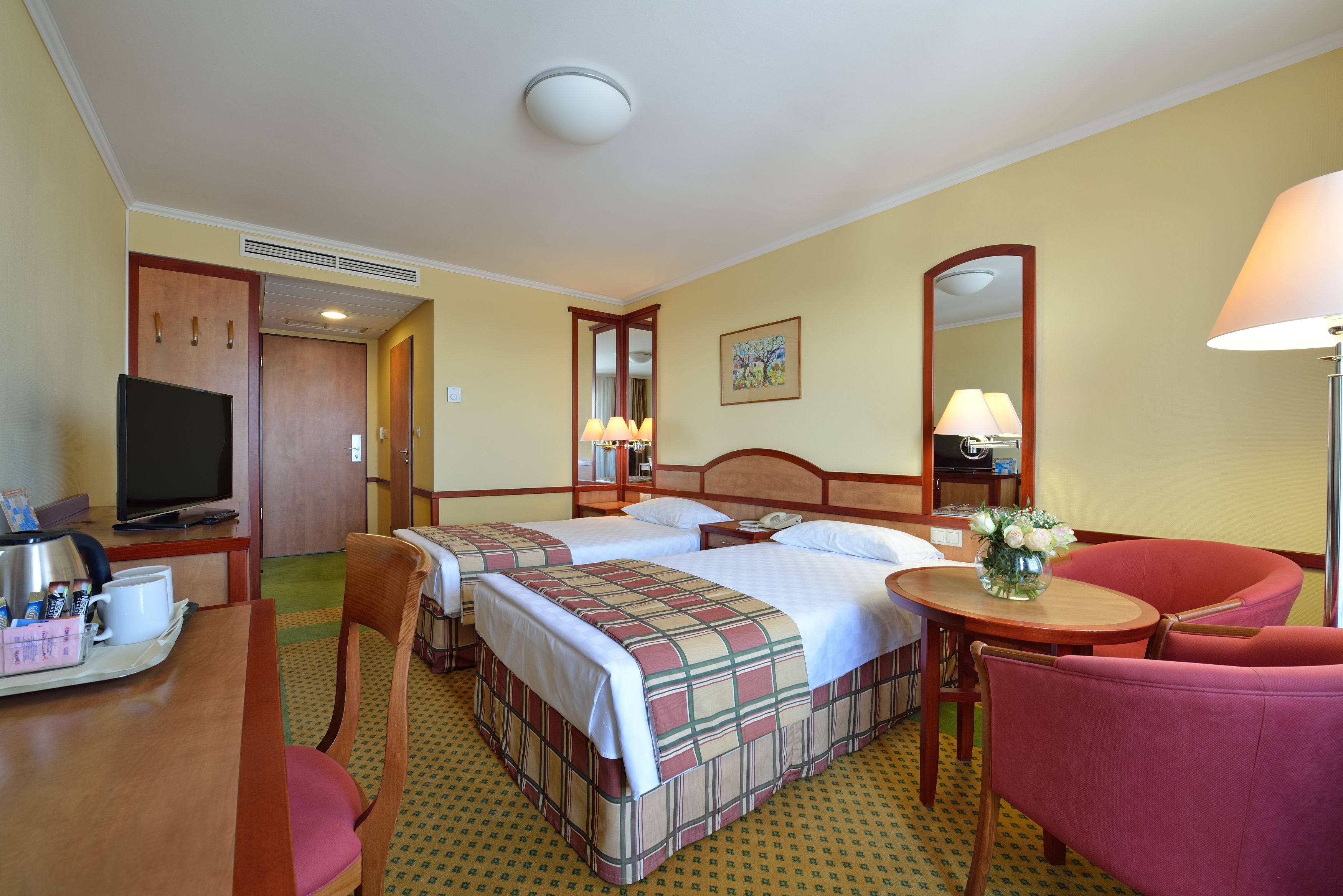 A hotel room with two beds, a TV, a desk with a coffee maker, and a chair.