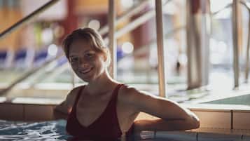 A woman in a red swimsuit in a pool area with metal railings and a tiled floor.