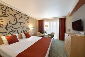 A hotel room with a large bed, a desk with a chair, a TV, and a dresser. - Danubius Hotel Bük (Buk)