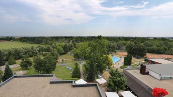 Eine Dachterrasse mit Blick auf eine angelegte Grünfläche, darunter ein Schwimmbecken, Liegestühle und ein Tennisplatz.