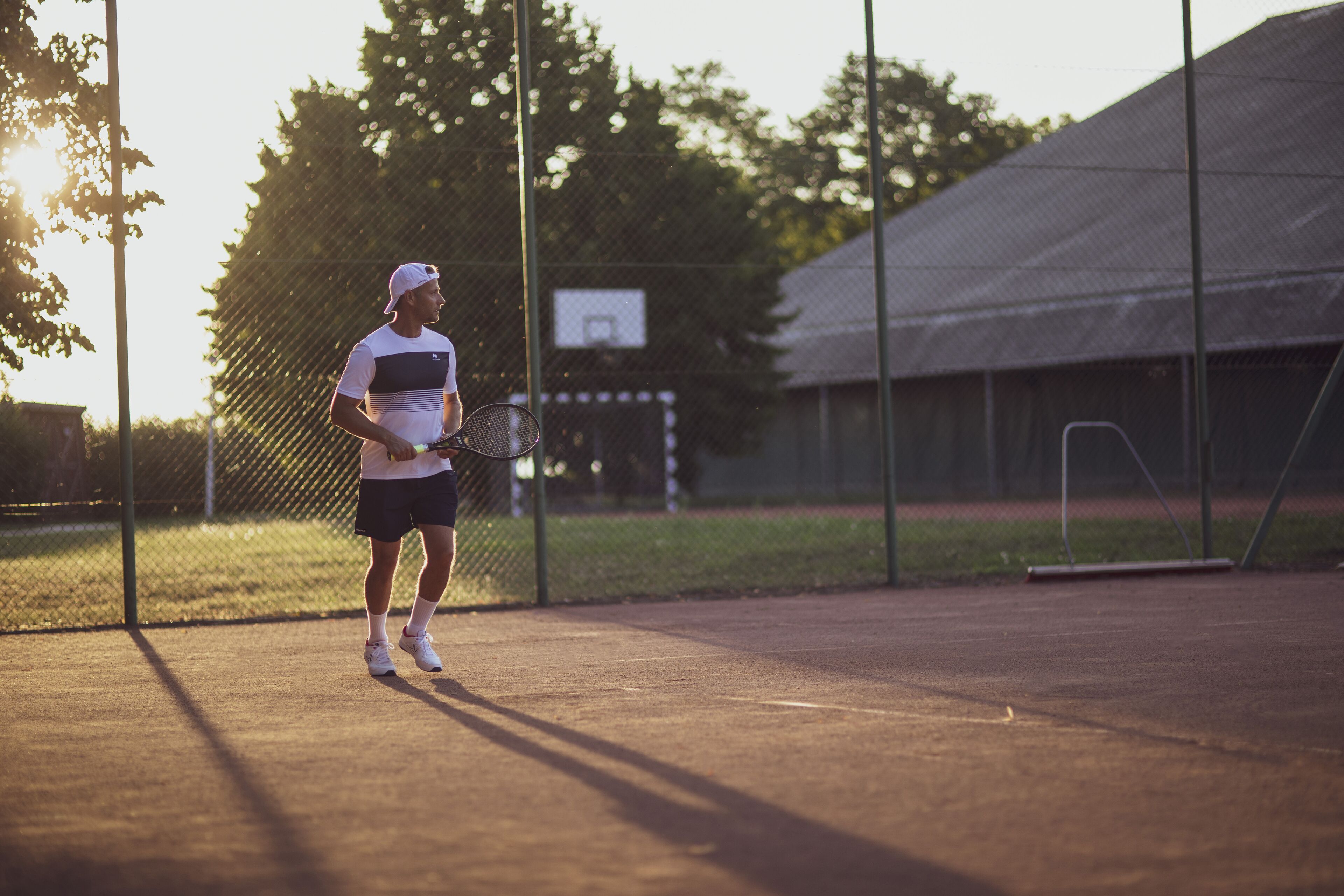 Una cancha de tenis con una red, un aro de baloncesto y un edificio al fondo.