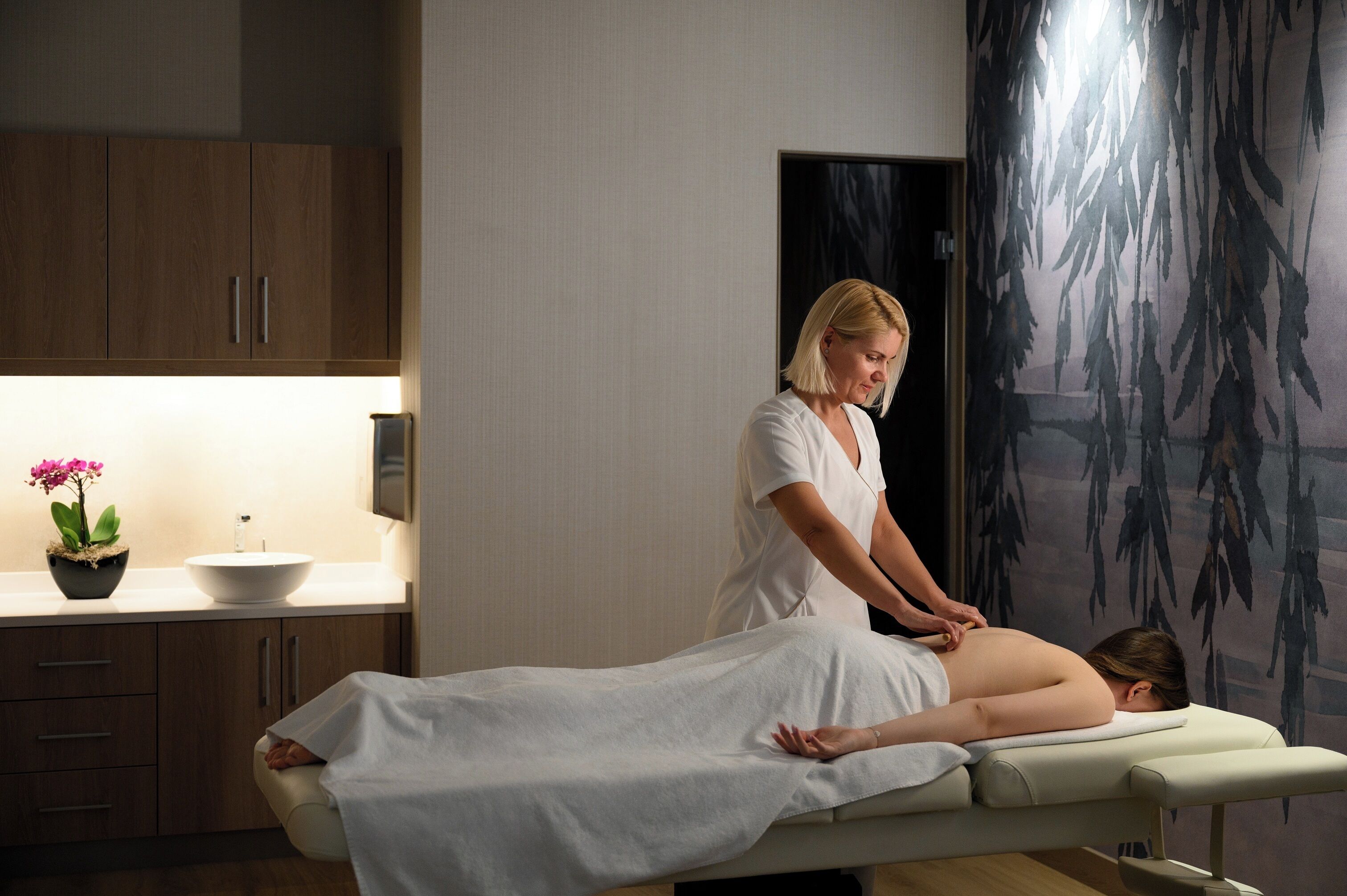A massage therapy room with a wooden cabinet, a sink, and a decorative wall with hanging elements.