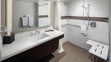 A modern bathroom with a large mirror, a sink, a shower, and a small table.
