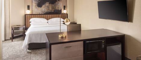 Una habitación de hotel con cama, mesita de noche, lámpara, televisor y minibar.